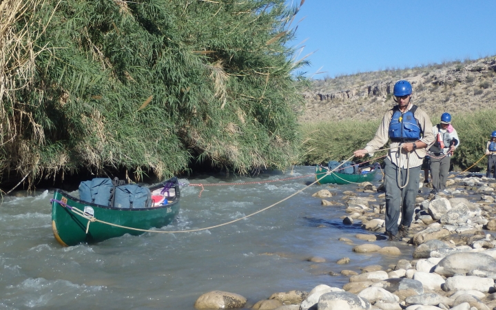 a person uses a rope to maneuver a canoe in water while walking along the rocky shore